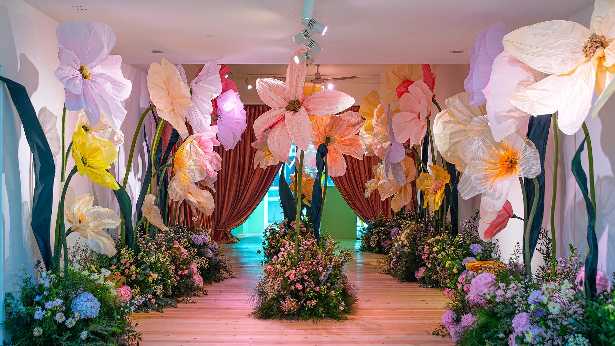 Immersive bespoke floral installation featuring oversized paper flowers and naturalistic ground arrangements creating fantastical walkway, showcasing Amaranté London's artistic approach to original custom floral design for extraordinary event experiences - Amarante London